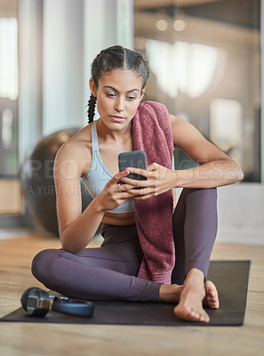 Buy stock photo Full length shot of an attractive young female athlete checking her phone while sitting in the gym