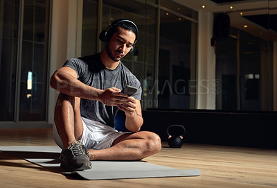 Buy stock photo Full length shot of a handsome young male athlete checking his phone while sitting in the gym
