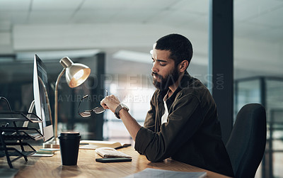 Buy stock photo Shot of a young businessman checking the time during a late night in a modern office