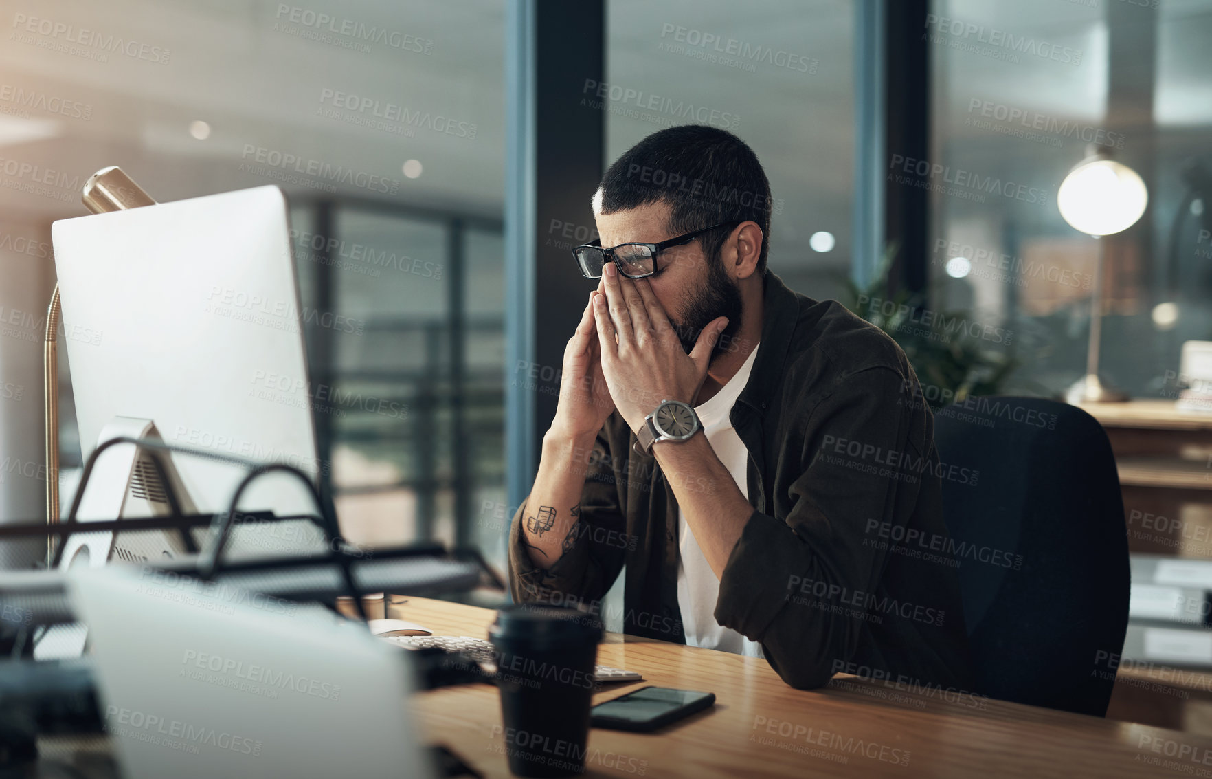 Buy stock photo Shot of a young businessman feeling stressed while working late at night in a modern office