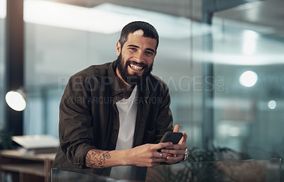Buy stock photo Shot of a young businessman using a smartphone during a late night in a modern office
