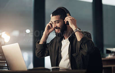 Buy stock photo Shot of a young businessman using a laptop and headphones during a late night at work