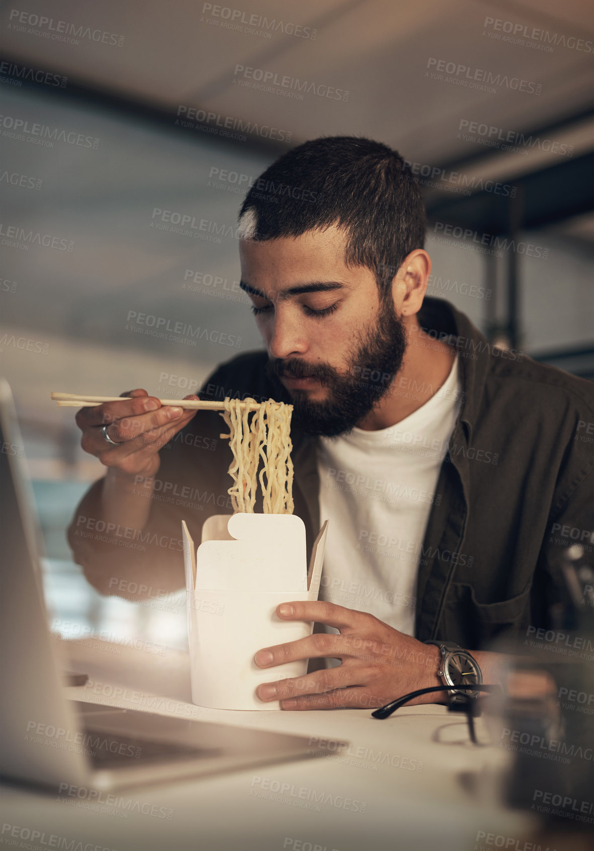 Buy stock photo Shot of a young businessman having takeout and using a laptop during a late night at work