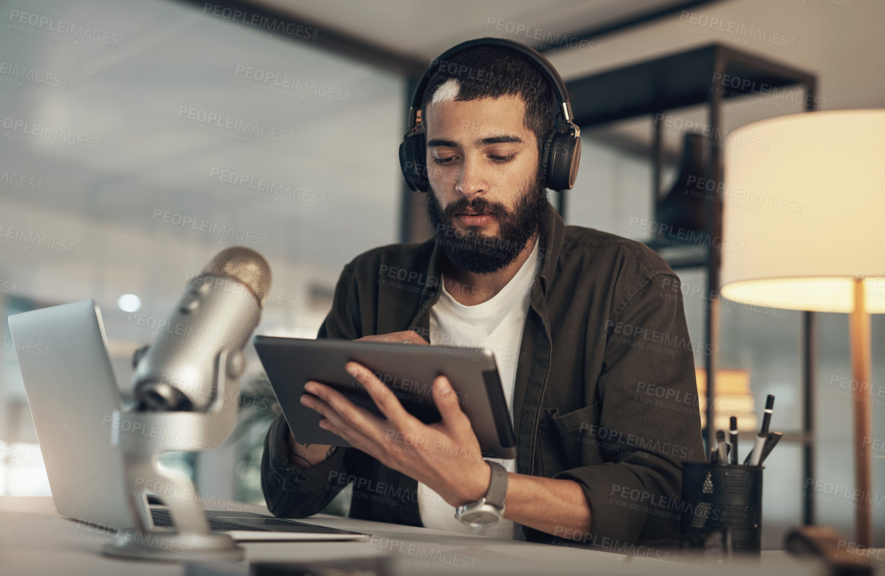 Buy stock photo Shot of a young man using a headset, microphone and digital tablet during a late night at work