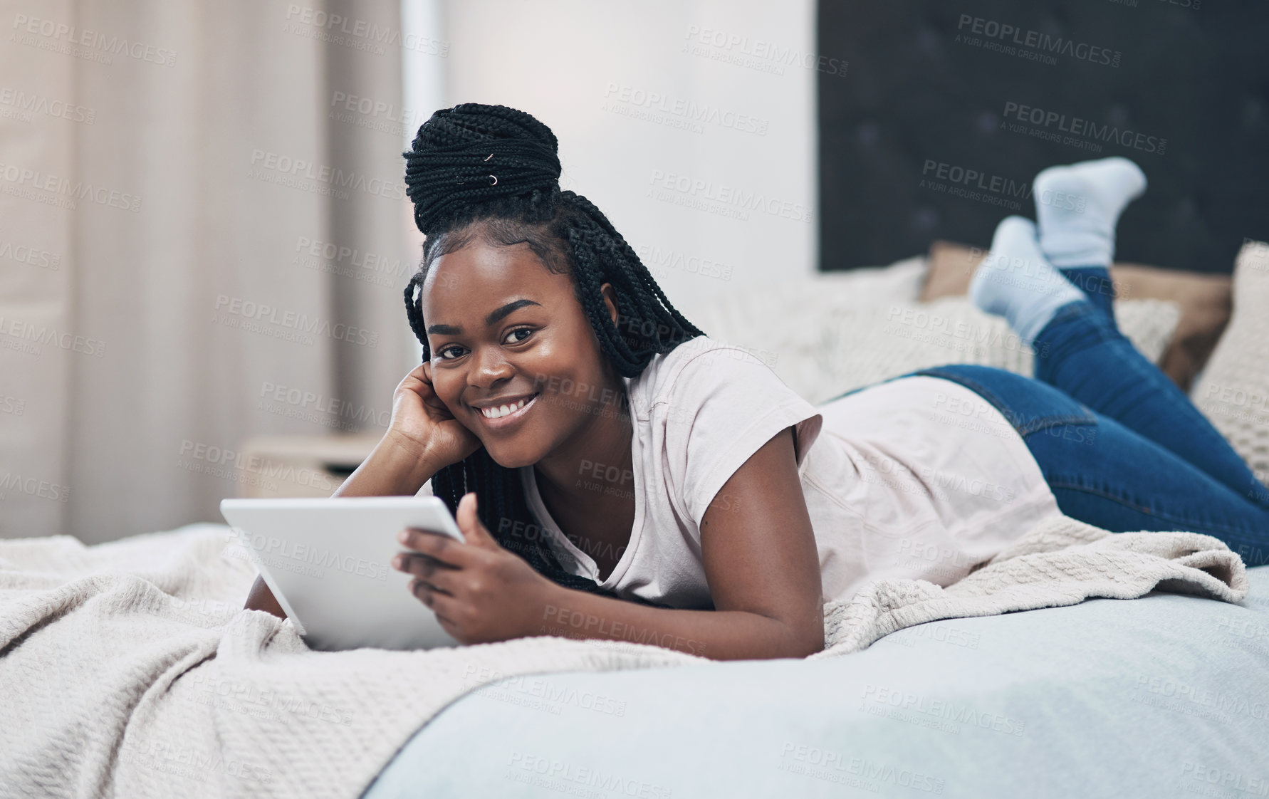Buy stock photo Shot of a young woman using a digital tablet while relaxing on her bed at home
