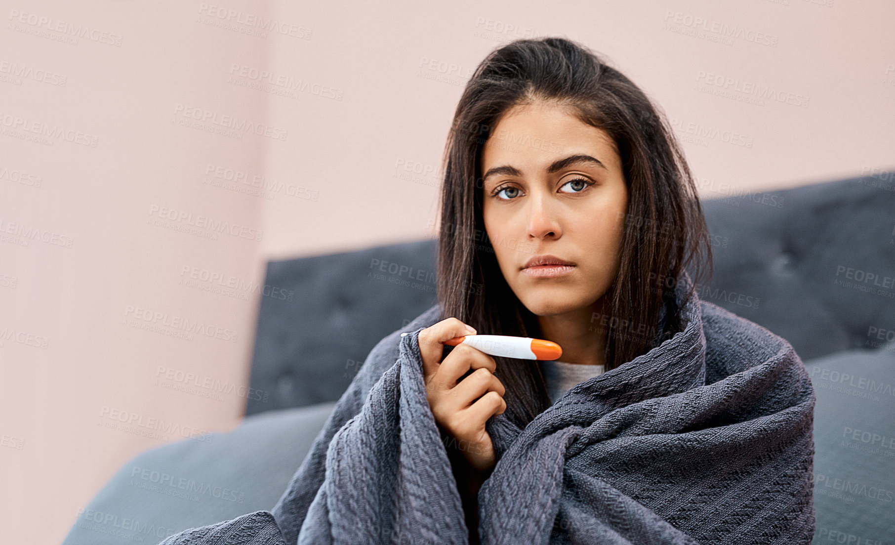 Buy stock photo Shot of a young woman taking her temperature while recovering from an illness in bed at home