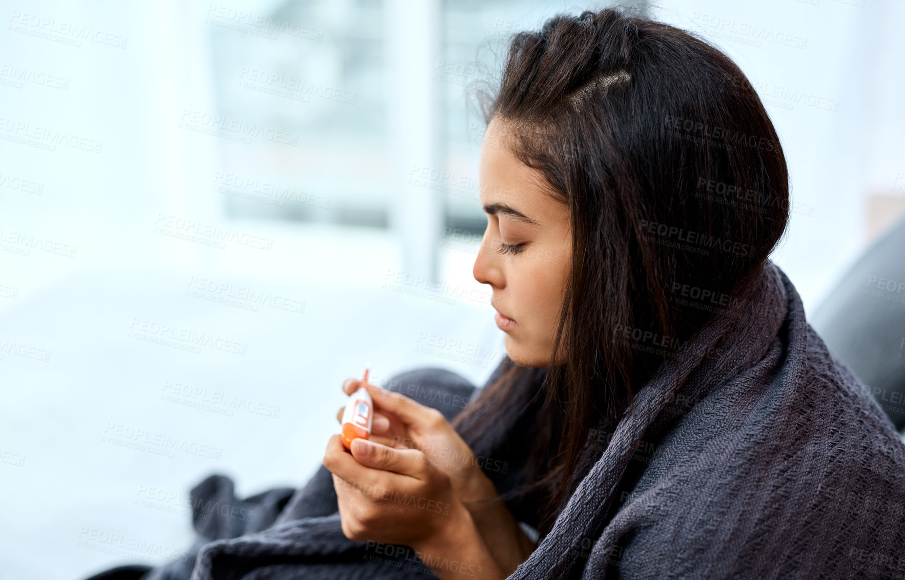 Buy stock photo Shot of a young woman taking her temperature while recovering from an illness in bed at home