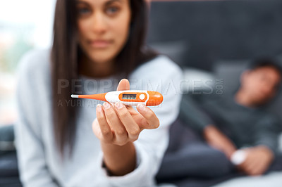 Buy stock photo Shot of a young woman using a thermometer while recovering from an illness with her husband at home