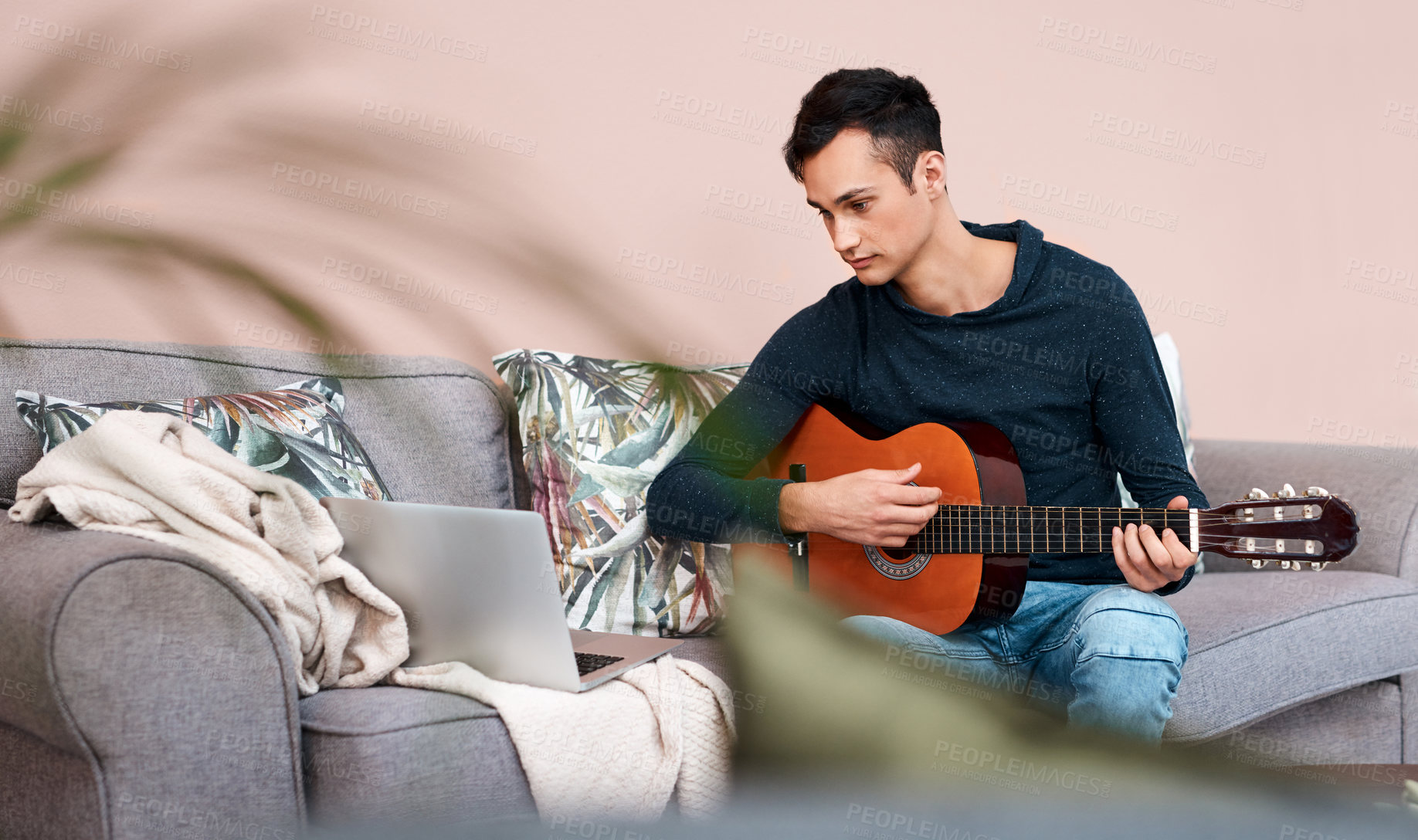 Buy stock photo Shot of a young man using a laptop while playing the guitar at home