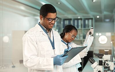 Buy stock photo Shot of a young scientist writing notes while working alongside a colleague in a lab