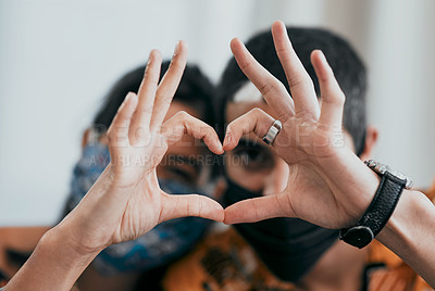 Buy stock photo Shot of a masked young couple making a heart shaped gesture with their hands at home