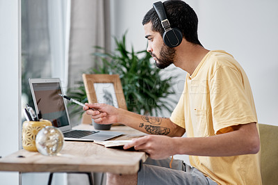 Buy stock photo Shot of a young man using a laptop and headphones while working from home