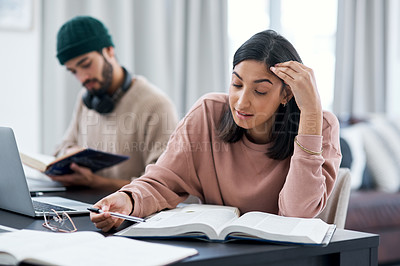 Buy stock photo Shot of a young woman looking stressed while working from home with her husband in the background