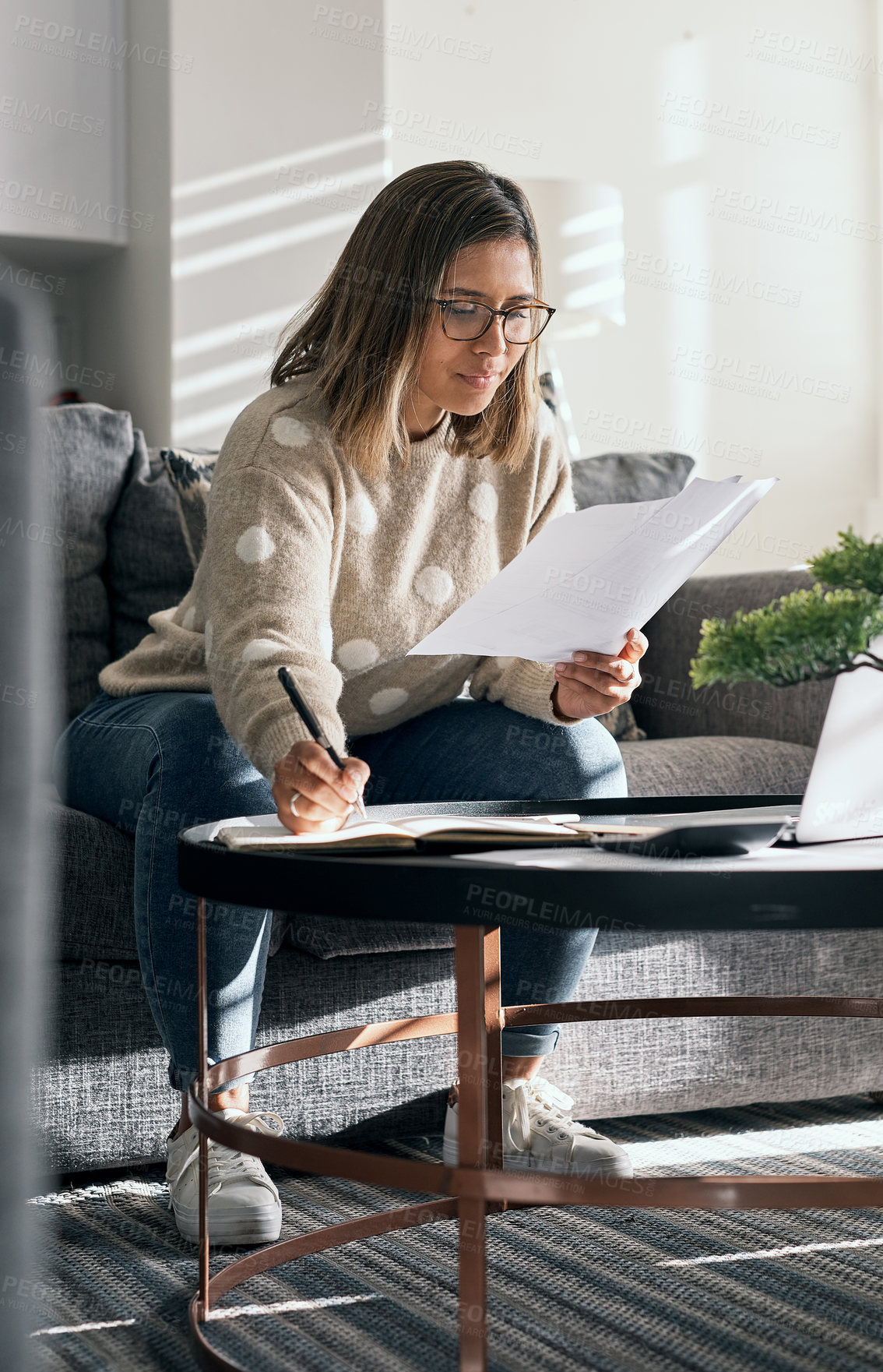 Buy stock photo Shot of a young woman looking at paperwork while working from home