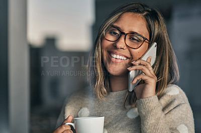 Buy stock photo Shot of a woman holding a cup of coffee while talking on her cellphone at home