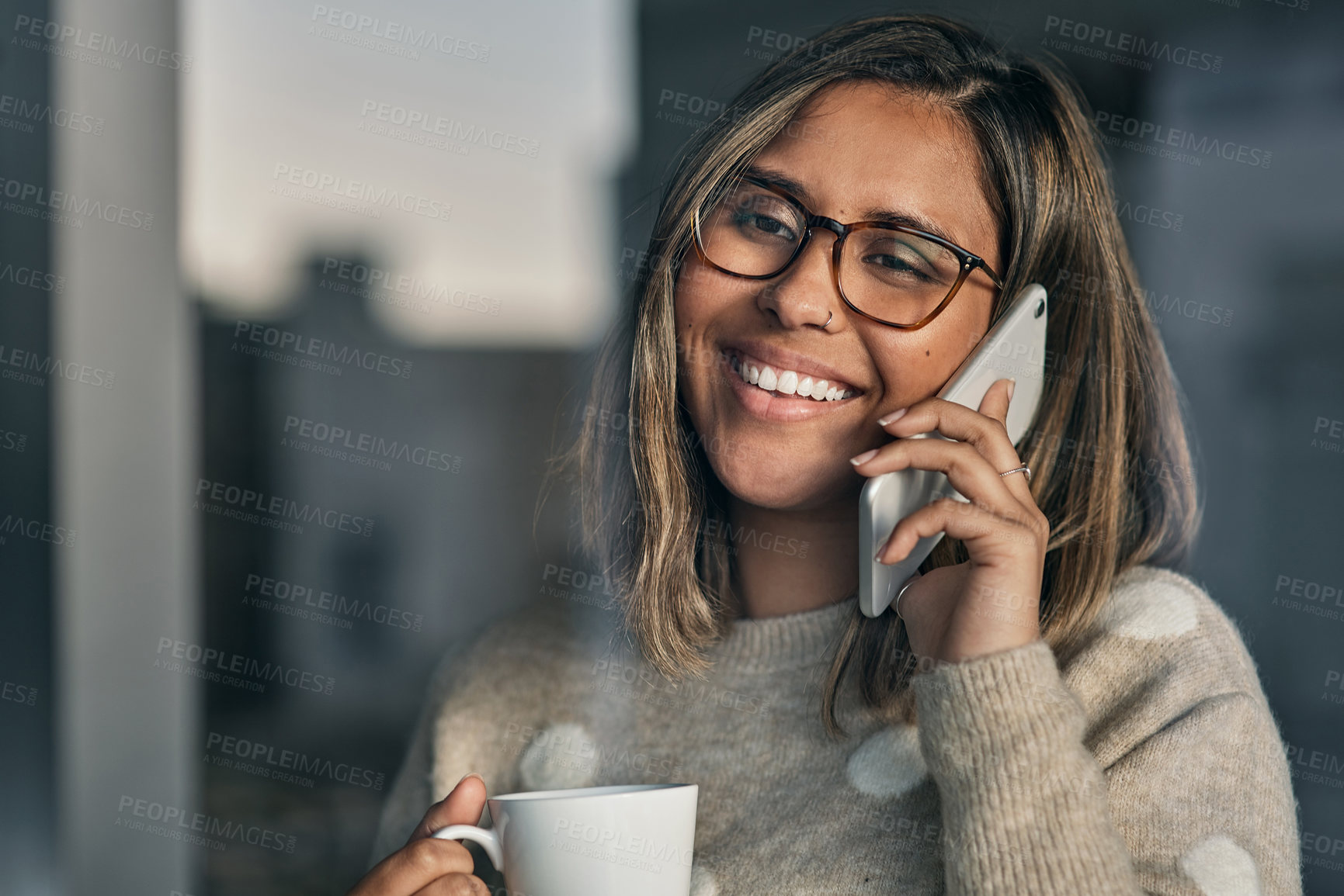 Buy stock photo Shot of a woman holding a cup of coffee while talking on her cellphone at home