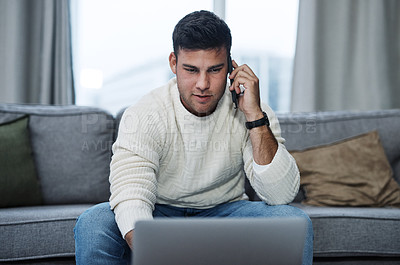 Buy stock photo Shot of a young man using a laptop and smartphone while working from home