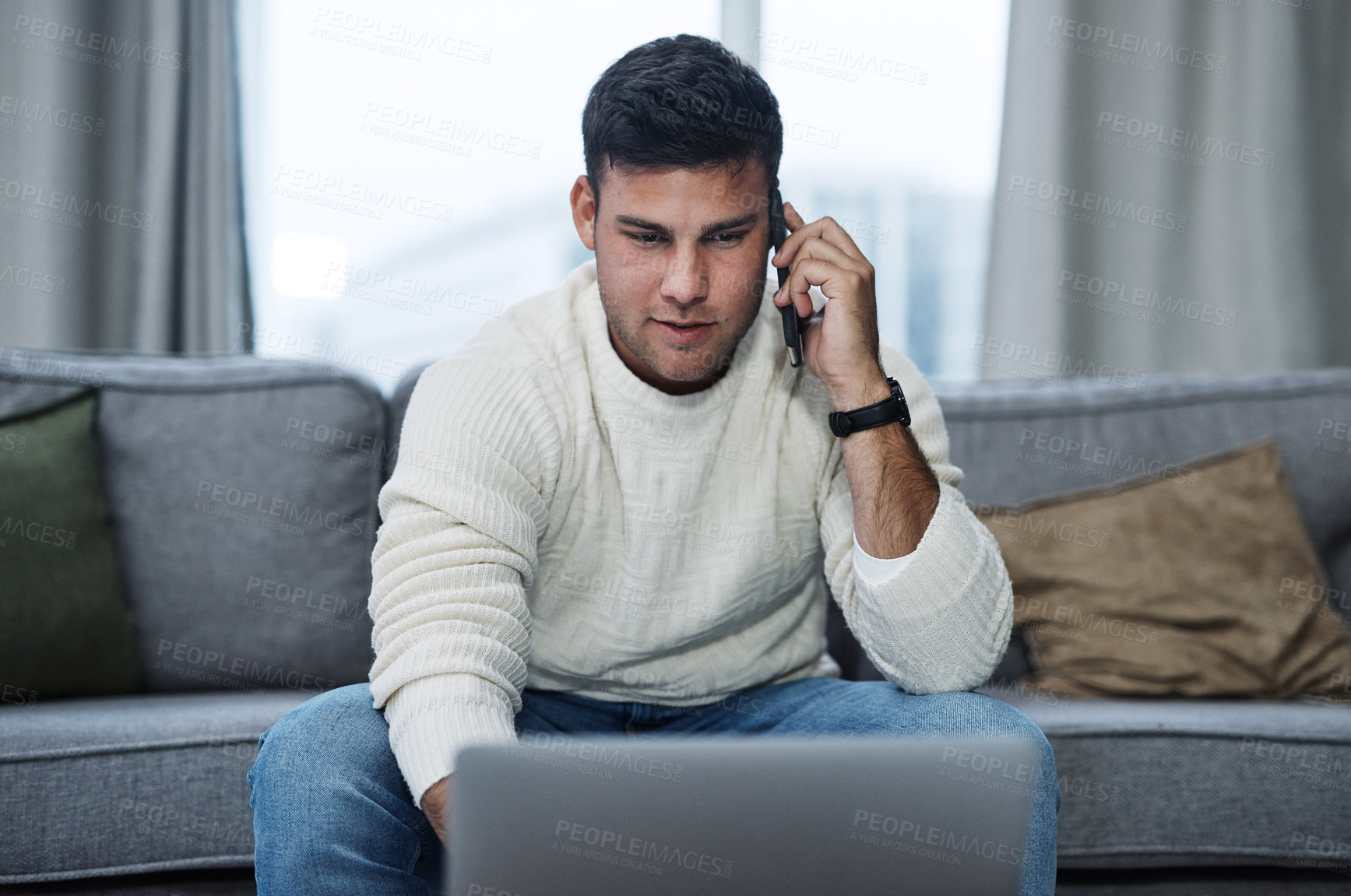 Buy stock photo Shot of a young man using a laptop and smartphone while working from home