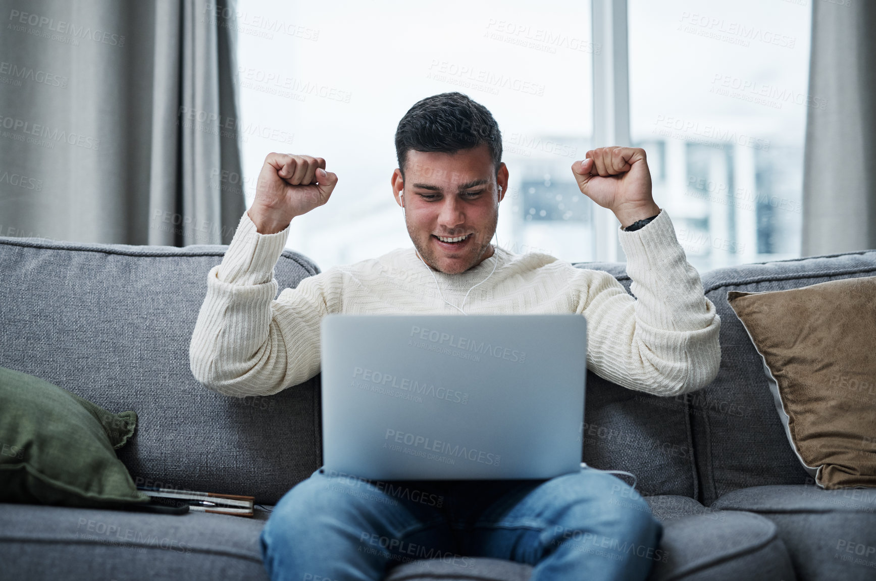 Buy stock photo Shot of a young man cheering while using a laptop on the sofa at home