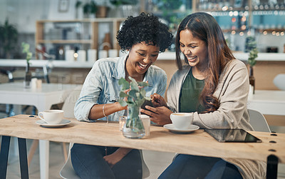 Buy stock photo Shot of two friends looking at something on a cellphone while sitting together in a coffee shop
