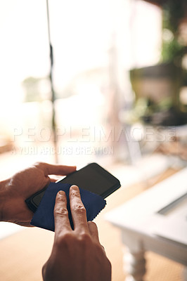 Buy stock photo Cropped shot of an unrecognisable man wiping a smartphone with a cloth at home