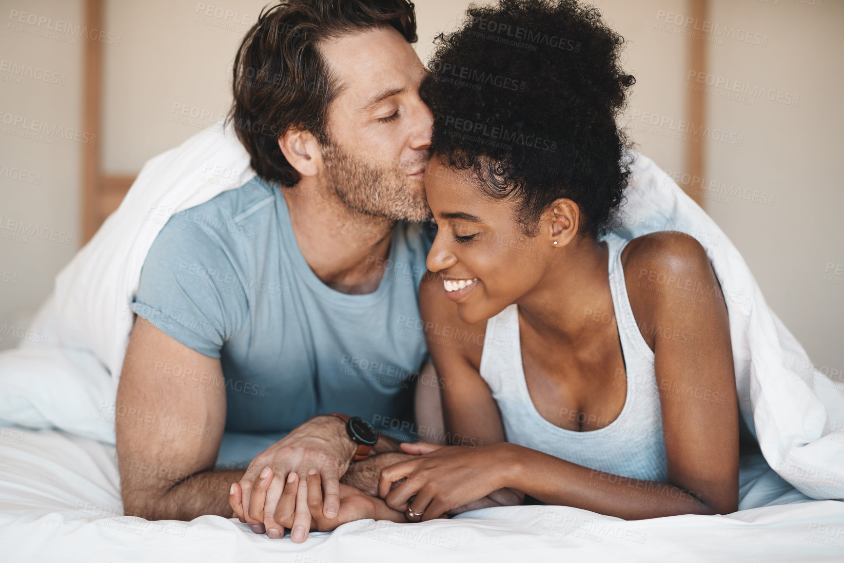 Buy stock photo Happy interracial couple, bed and morning kiss in relax or bonding relationship at home. Man kissing woman on forehead in happiness or embrace for love or relaxing weekend together in the bedroom