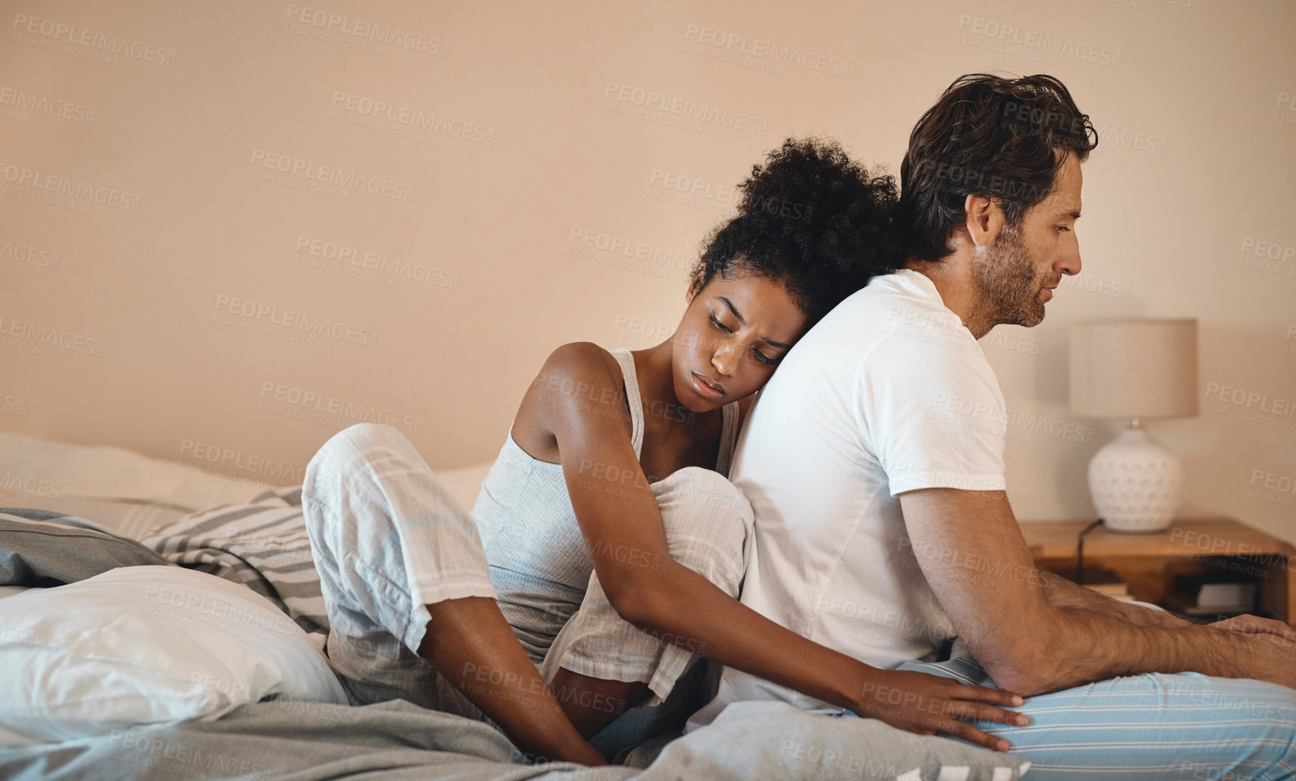 Buy stock photo Sad, frustrated and unhappy man and woman hugging after a breakup in their bedroom. Upset, annoyed and depressed male getting support with his wife. Interracial couple cuddling to comfort husband.
