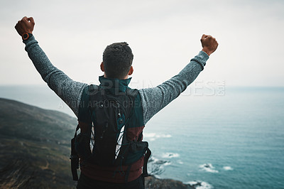 Buy stock photo Rearview shot of a young man standing with his arms outstretched while hiking on a mountain