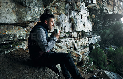 Buy stock photo Shot of a young man drinking coffee while hiking through the mountains