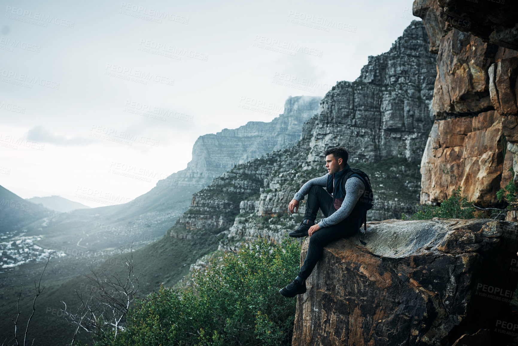 Buy stock photo Shot of a young man looking at the view while sitting on a mountain cliff