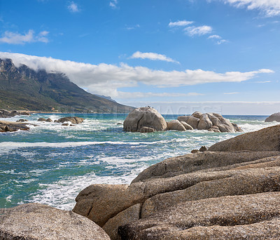 Buy stock photo A calming ocean view of the rocky coast of Camps Bay in Cape Town, South Africa. Boulders at a beach with the tide and current coming in and Table Mountain on the horizon. Tidal waves washing ashore