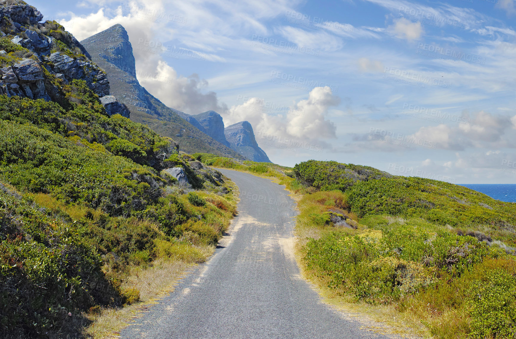 Buy stock photo Asphalt road on Table Mountain with cloudy blue sky. Landscape of countryside roadway for traveling on mountain pass along a beautiful scenic nature drive with lush shrubs in Cape Town, South Africa