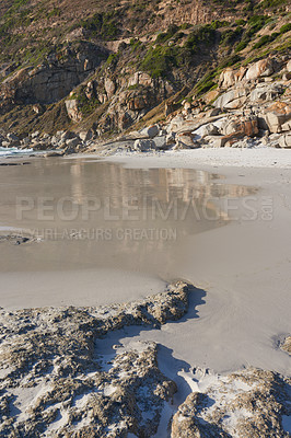 Buy stock photo A rocky coastline at a beach in Cape Town with mountains in the background and copyspace. View of a shore with rocks at the ocean. Rocky coast of mountain sea washing over beach sand on a cold day