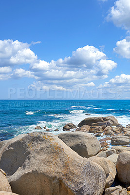 Buy stock photo Copyspace at sea with a cloudy blue sky background and rocky coast in Camps Bay, Cape Town, South Africa. Boulders at a beach shore across a majestic ocean. Scenic landscape for a summer holiday