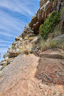 Buy stock photo Scenic of plants and shrubs growing on a rocky mountain slope with cloudy sky background. Rugged landscape of boulders on a cliff with hiking trails to explore on Lion's Head, Cape Town, South Africa