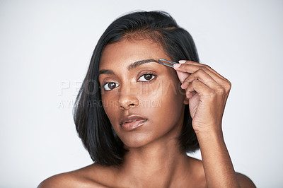 Buy stock photo Shot of a beautiful young woman tweezing her eyebrows against a white background