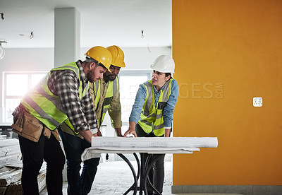 Buy stock photo Shot of a group of builders going over building plans at a construction site