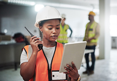 Buy stock photo Shot of a young woman using a digital tablet and walkie talkie while working at a construction site