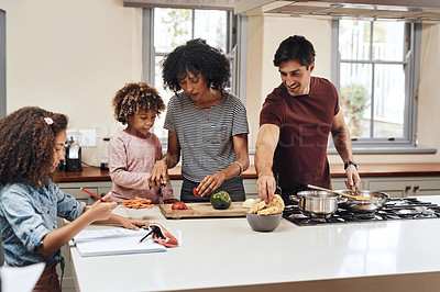 Buy stock photo Shot of a little girl doing her homework while the rest of her family is busy cooking