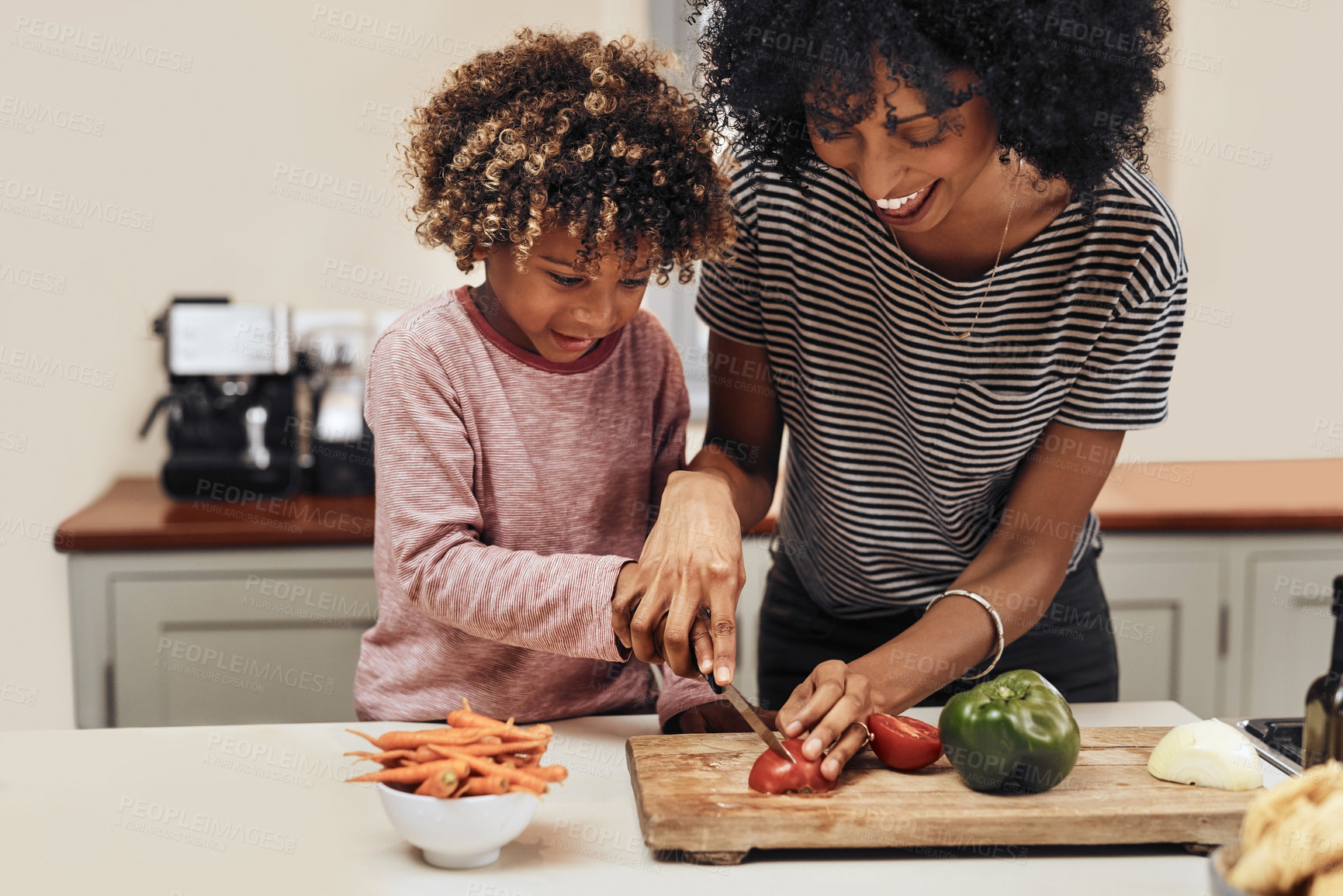 Buy stock photo Shot of a young boy cutting vegetables with the assistance of his mother