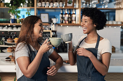 Buy stock photo Shot of two young women drinking coffee together while working in a cafe