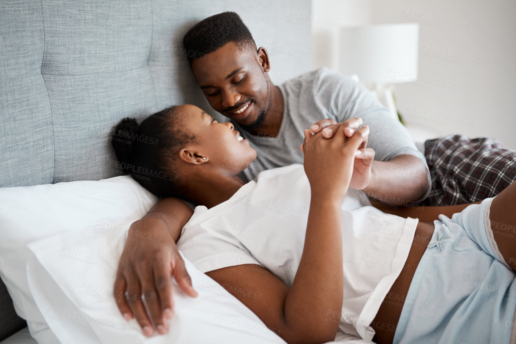 Buy stock photo Shot of an affectionate young couple relaxing on their bed together at home