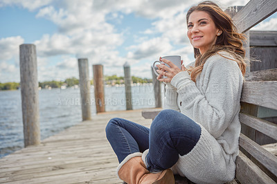 Buy stock photo Shot of a beautiful young woman enjoying a warm beverage while relaxing on a bench at a lake