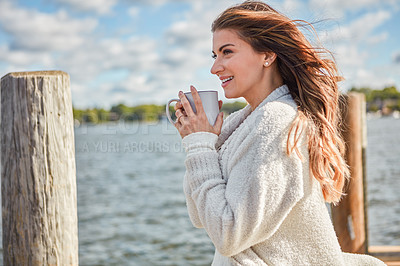 Buy stock photo Shot of a beautiful young woman enjoying a warm beverage on a pier at a lake