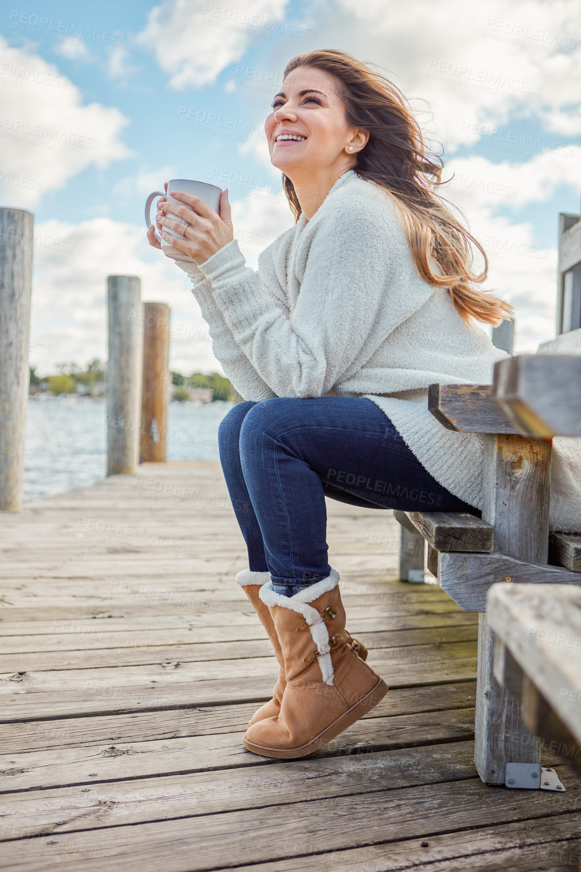 Buy stock photo Shot of a beautiful young woman enjoying a warm beverage while relaxing on a bench at a lake