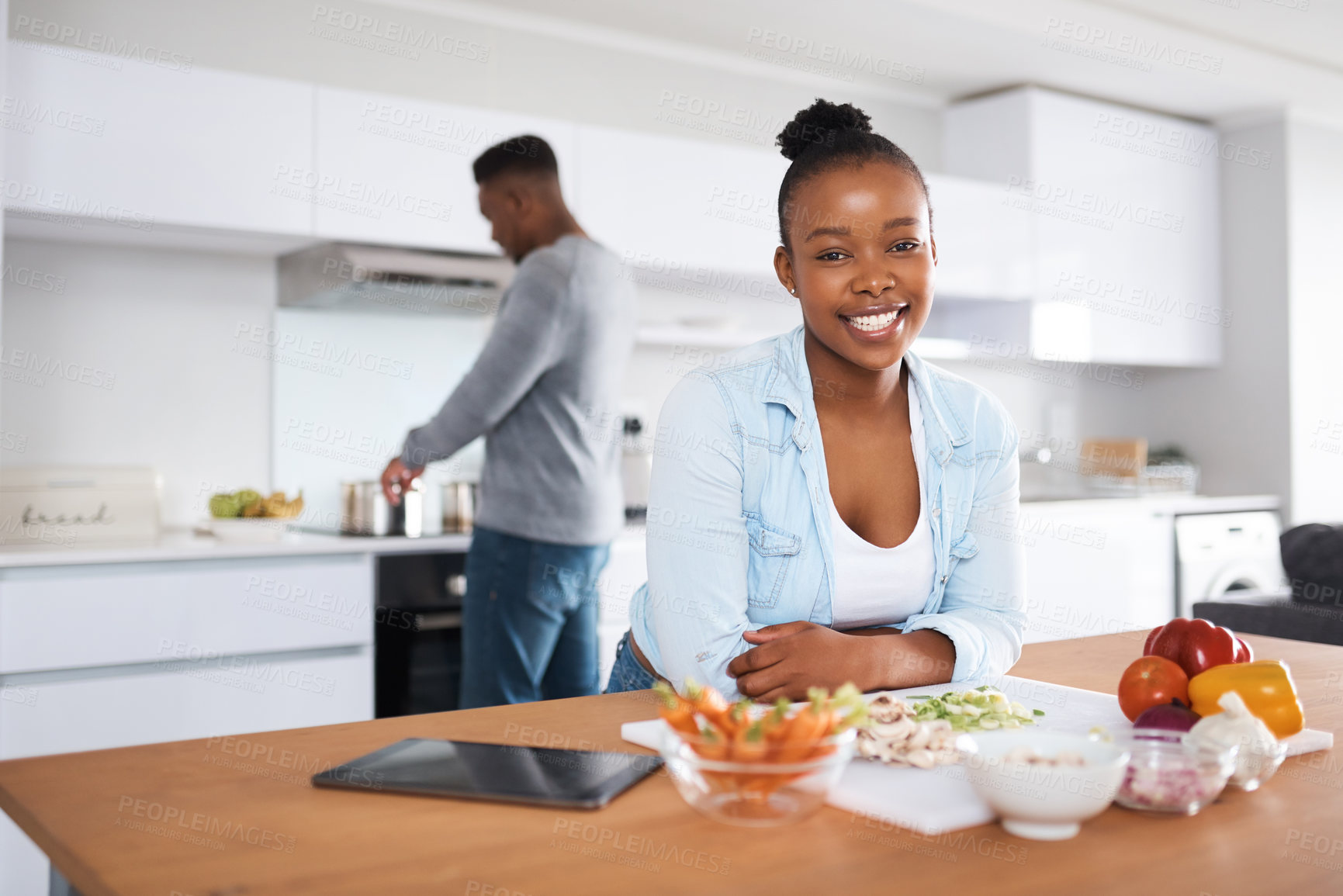 Buy stock photo Shot of a woman smiling at the camera while her boyfriend cooks in the background