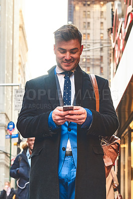 Buy stock photo Shot of a cheerful young man texting on his cellphone while standing in the busy streets of the city during the day