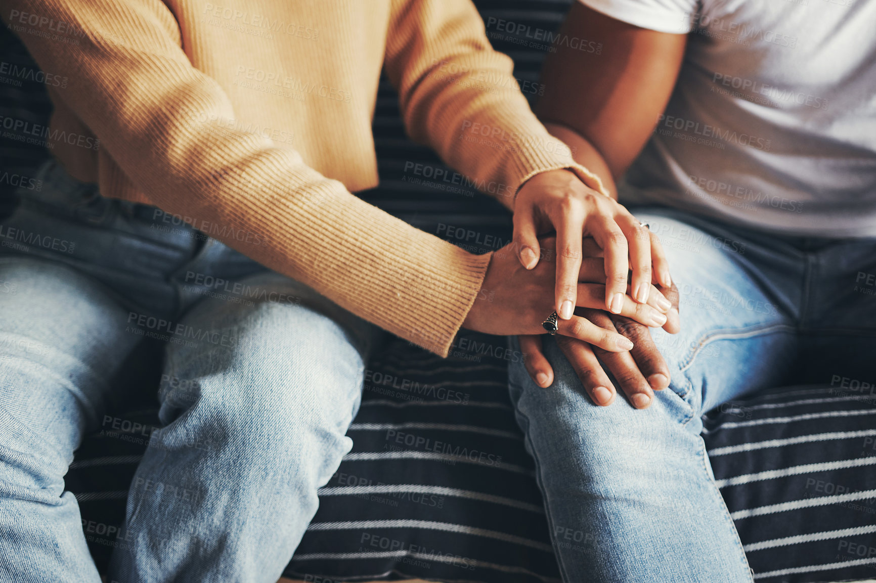 Buy stock photo Closeup shot of an unrecognisable couple holding hands while sitting together on a sofa at home