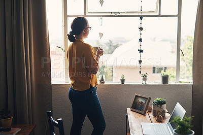 Buy stock photo Shot of a young woman having coffee and looking thoughtful while working from home