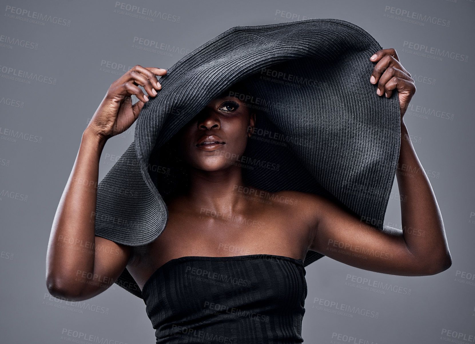 Buy stock photo Shot of a young woman wearing a oversized sunhat against a grey background